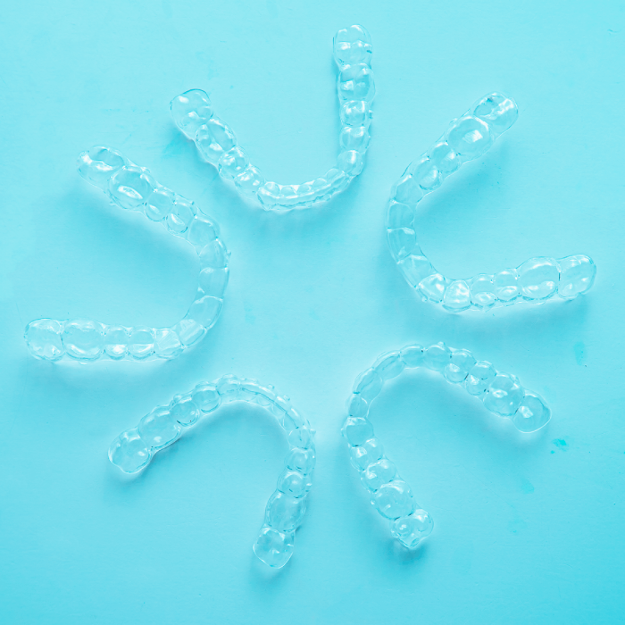 Five clear dental aligners arranged in a circular pattern on a light blue background.