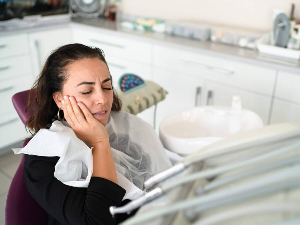 a woman in a dental clinic sitting on a dental chair while in tooth pain