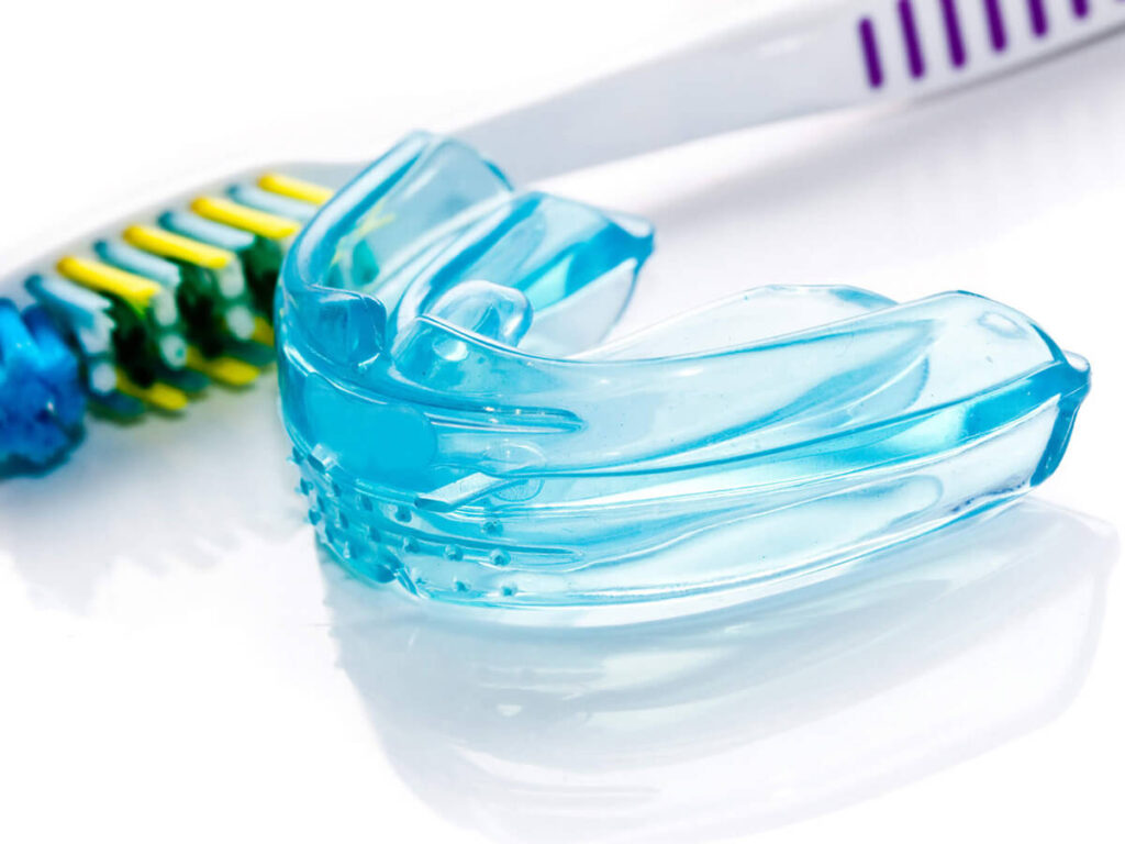 Show thumbnail preview A blue dental mouthguard is placed next to a toothbrush with colorful bristles on a white surface.